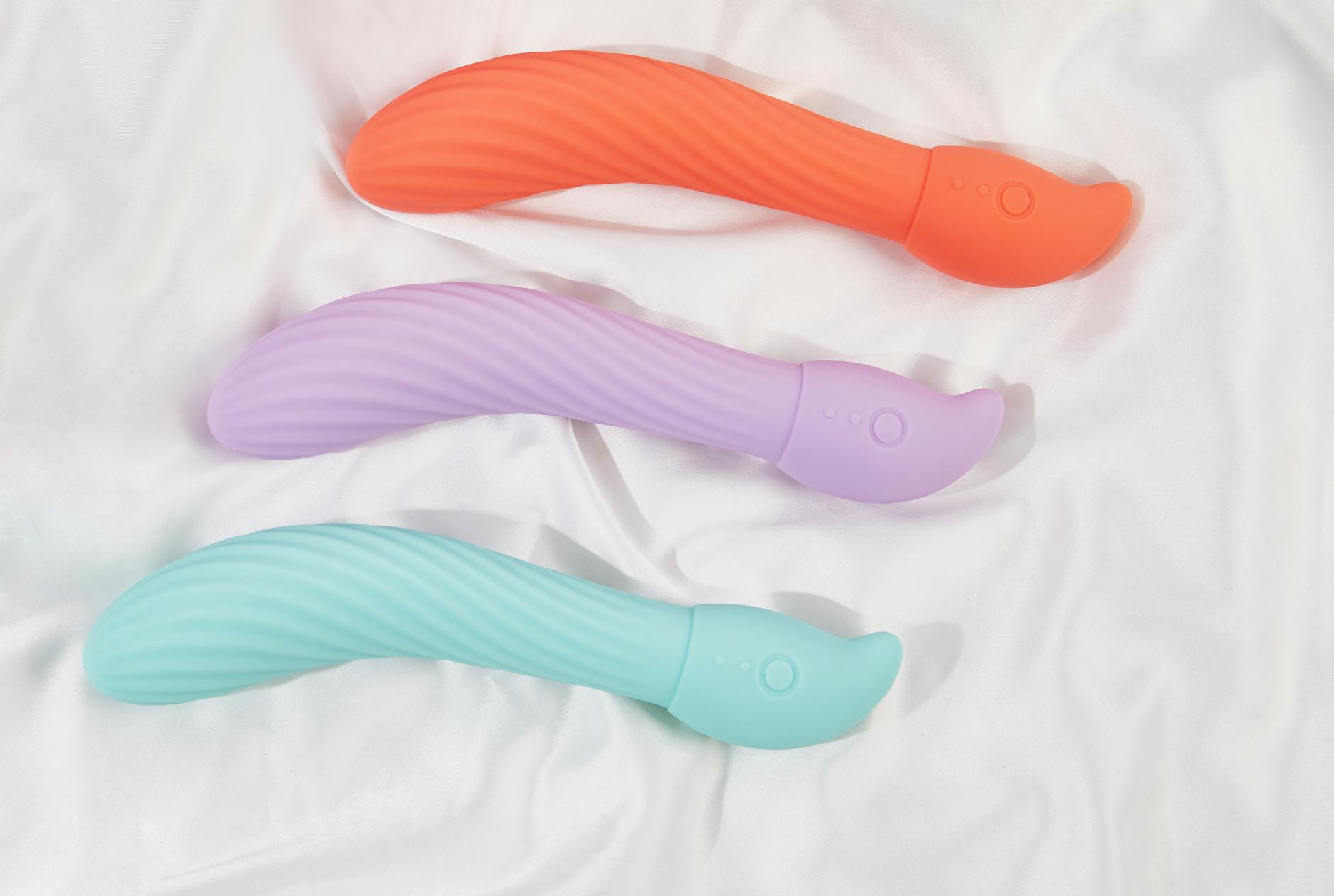 Three colorful vibrators arranged on white fabric, highlighting their smooth texture and design variations