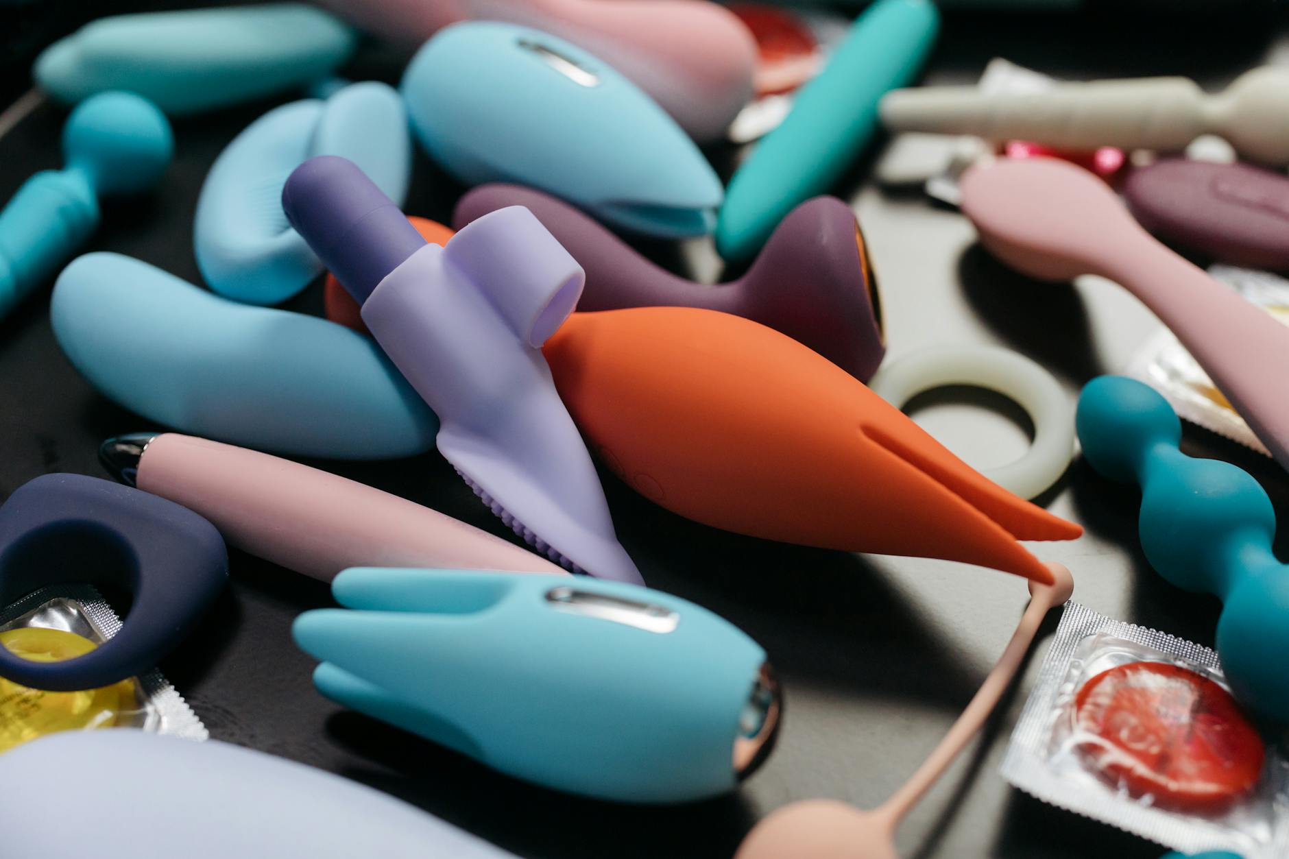 Woman holding blue and pink vibrators in contemplative manner against purple background