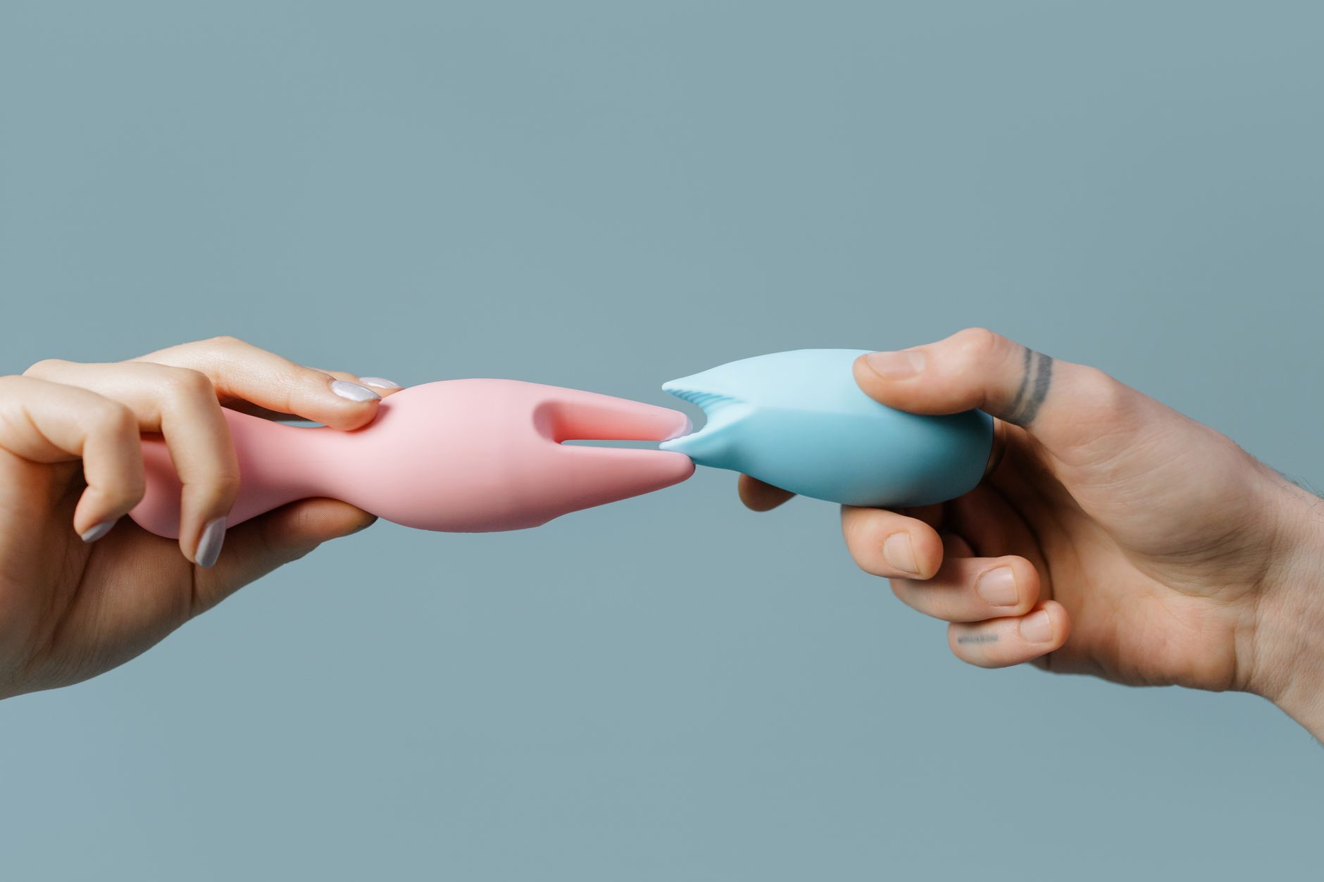 Woman holding blue and pink silicone vibrators in a contemplative pose