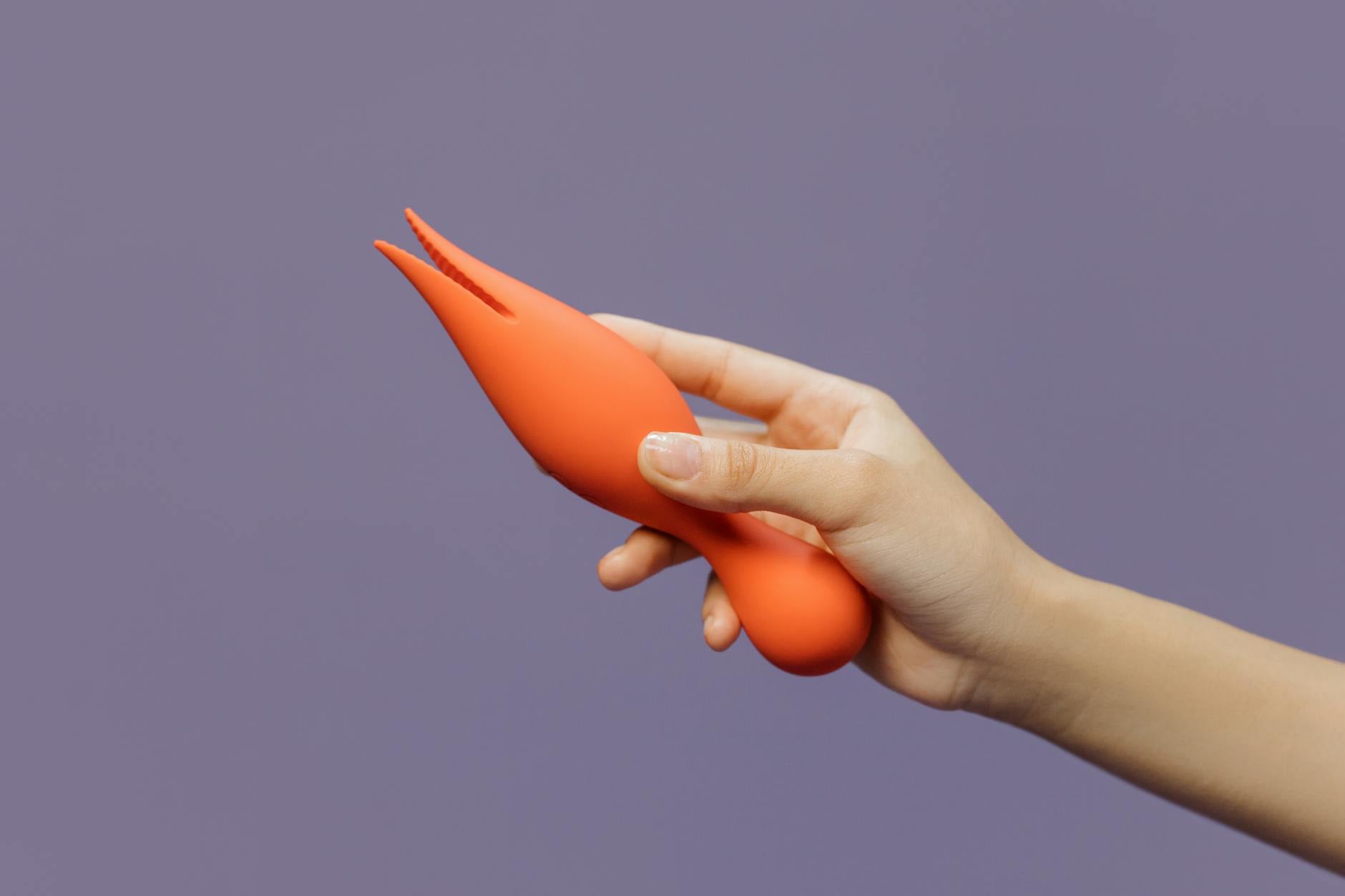 Hand holding a vibrator against a minimalist purple background, symbolizing intentional, pressure-free pleasure.