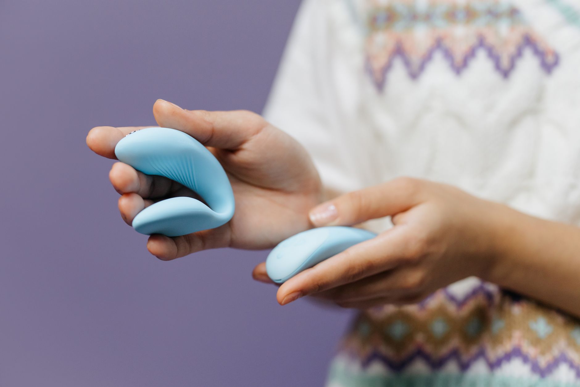 Hands holding a sleek blue clitoral vibrator, representing intentional pleasure and desire.