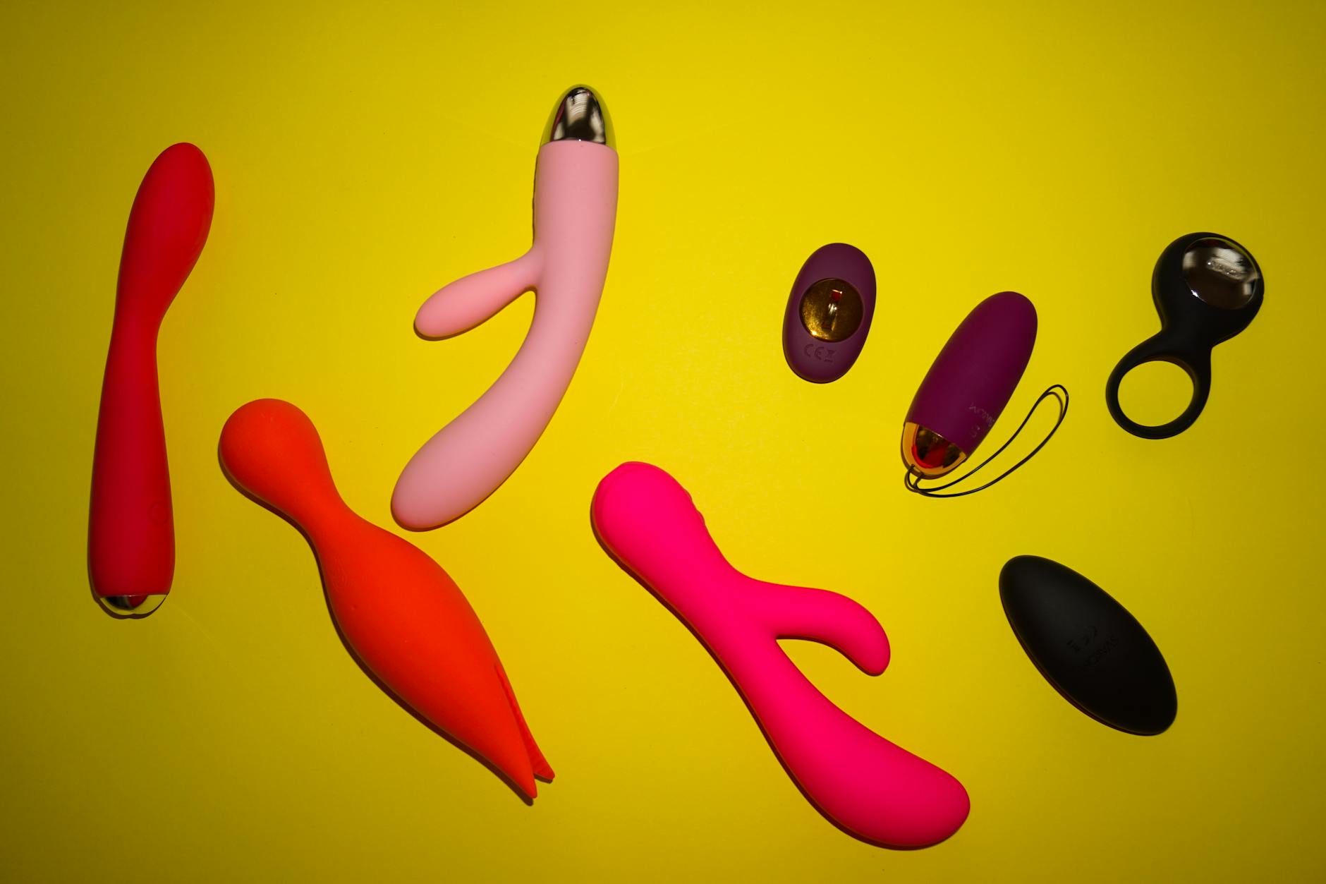 Two hands holding pink and blue silicone vibrators against a pastel background, representing shared pleasure and compromise